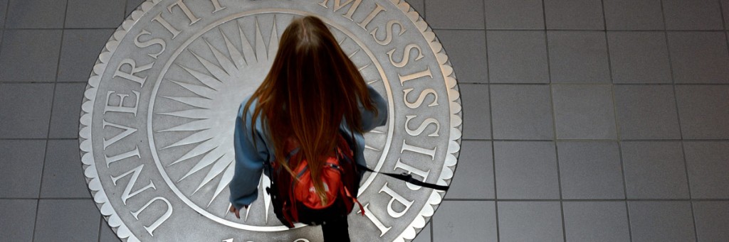 Student wearing a backpack walking over the seal of the University of Mississippi engraved into the floor.